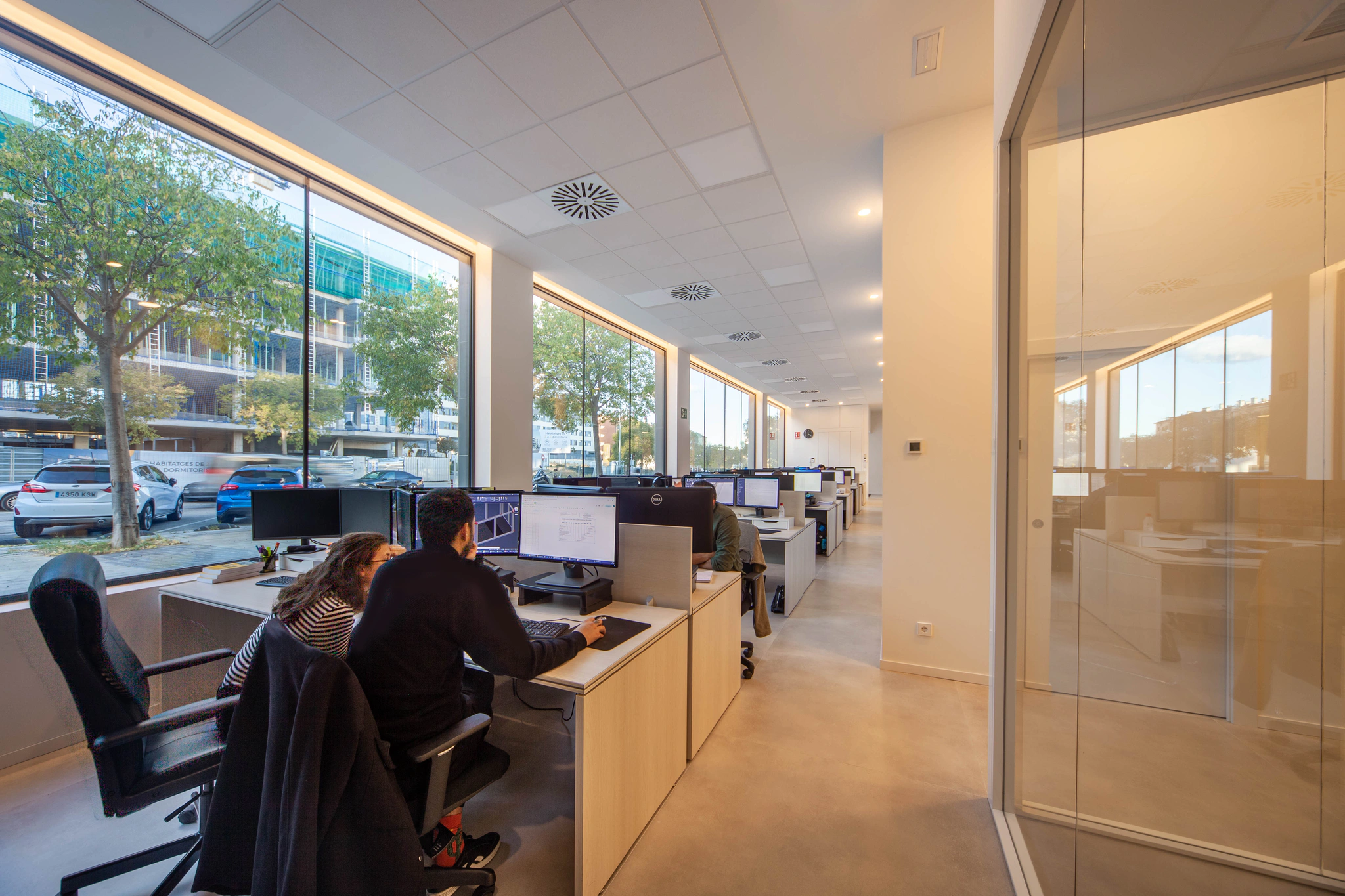 Fila de puestos de trabajo del equipo de producción BIM de A3D junto al ventanal, con dos especialistas revisando un modelo en pantalla.