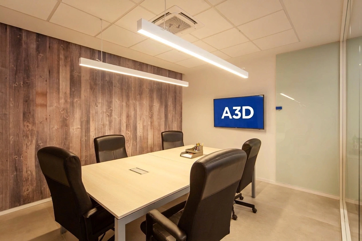 Sala de reuniones del despacho de A3D: mesa de trabajo, pantalla grande en la pared con el logotipo de A3D y revestimiento de madera