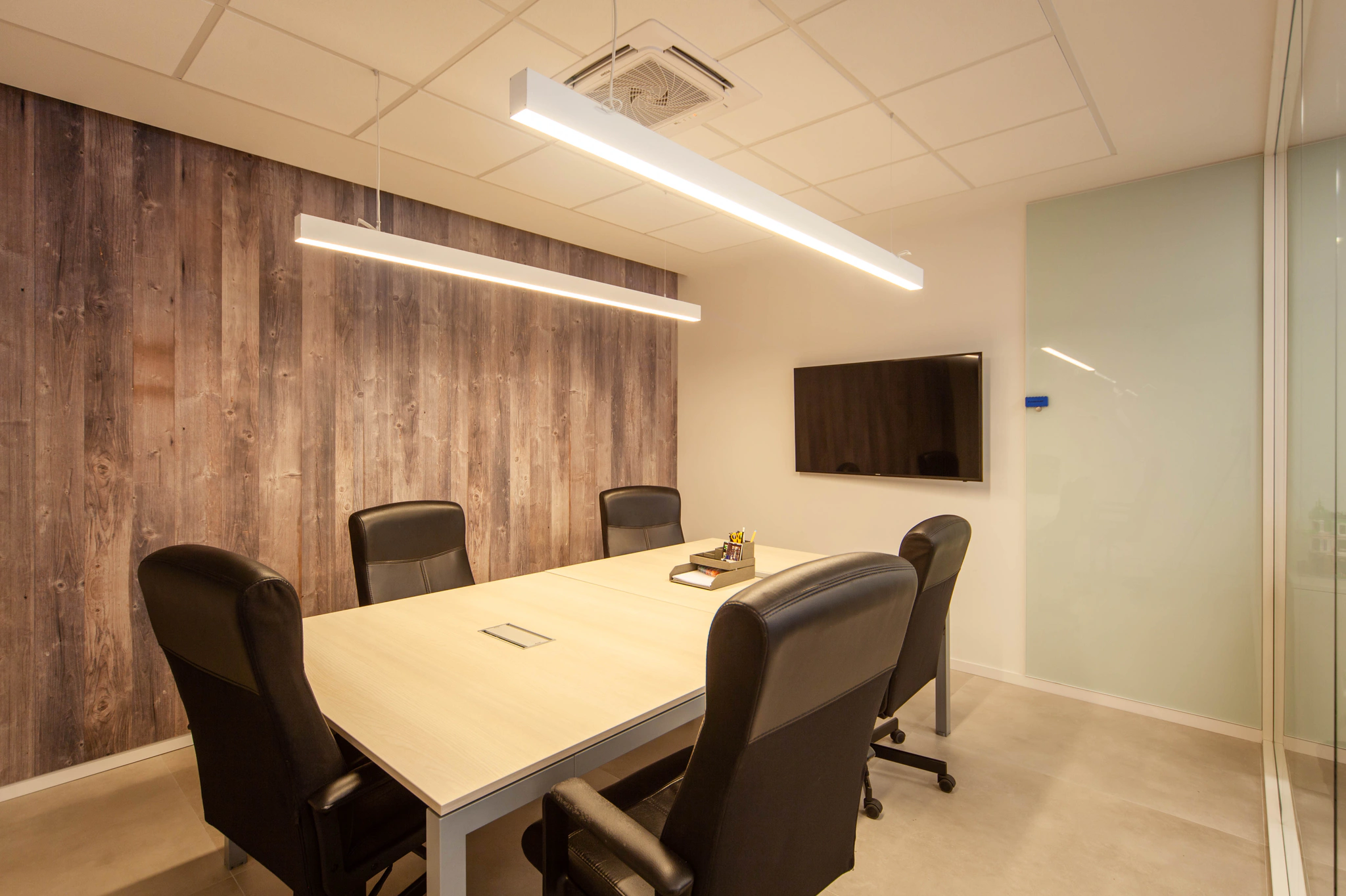Sala de reuniones de A3D con mesa para seis, pantalla grande en la pared y revestimiento de madera.